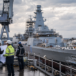 Representative image: Engineers review plans beside a naval vessel under construction, reflecting Babcock International Group’s Type 31 frigate cost challenge, defence execution risk, and broader UK shipbuilding strategy.