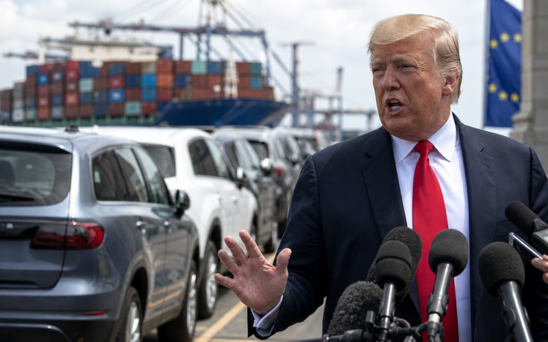 Representative image of United States President Donald Trump addressing reporters as imported cars and shipping containers frame the renewed United States–European Union auto tariff dispute, after Washington threatened to raise tariffs on European Union cars and trucks to 25 per cent.